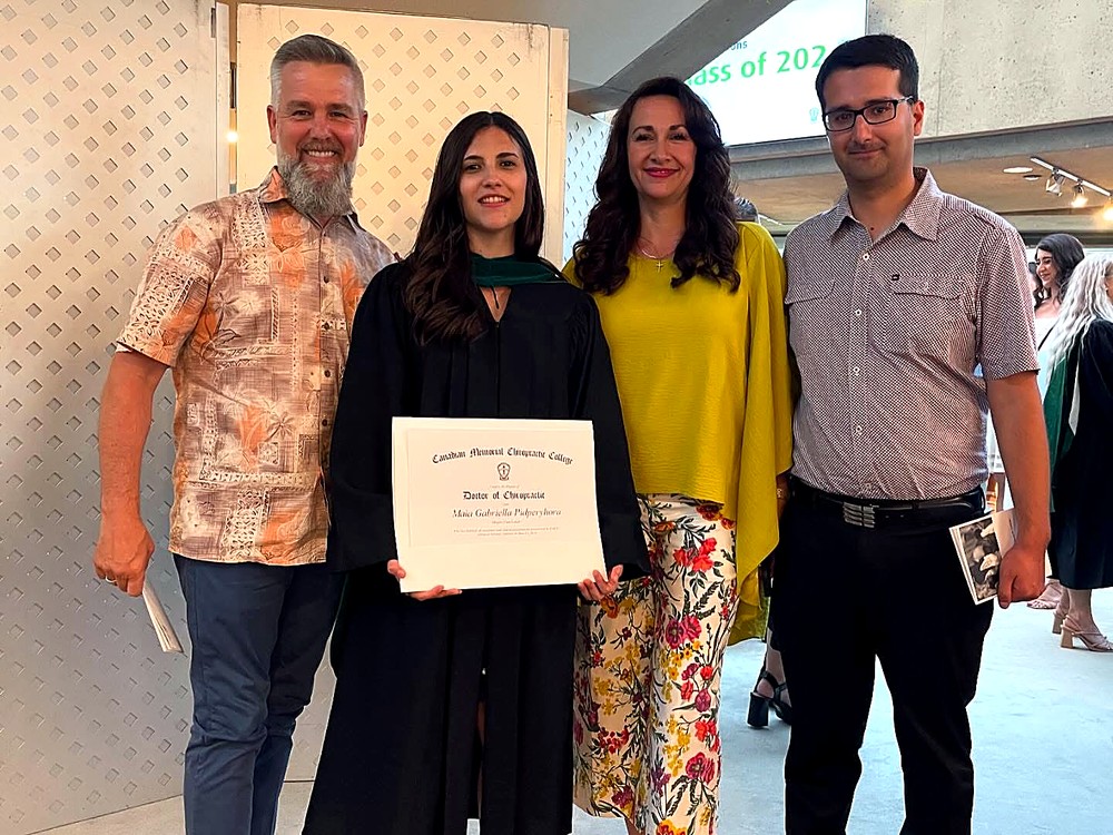 Dr. Maia on graduation day at CMCC in Toronto, holding her Doctor of Chiropractic degree, with her family