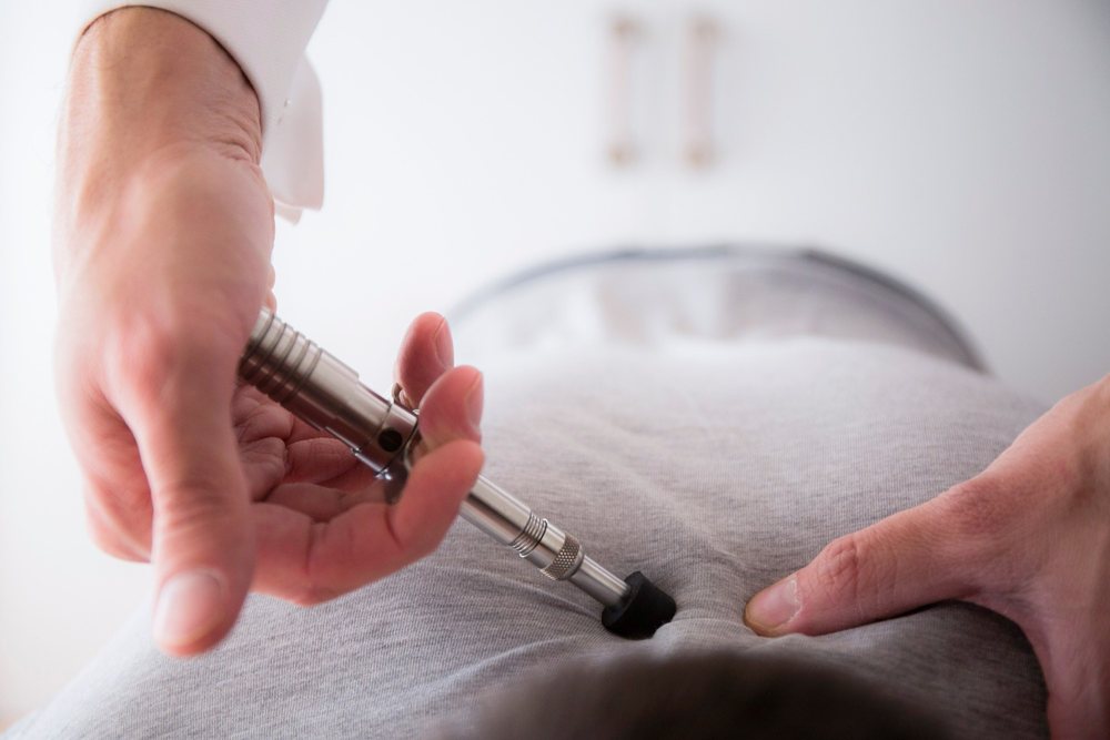 An Activator adjusting instrument held in the hand, its rubber tip on a patient's back