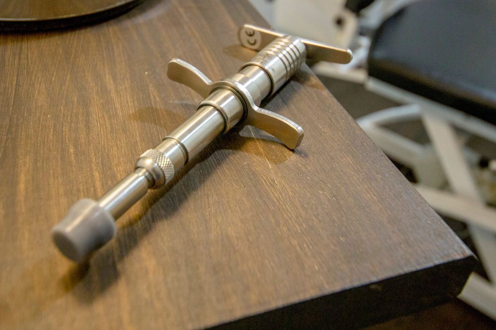 A stainless steel Activator adjusting instrument with a rubber tip, resting on a wooden table in a treatment room
