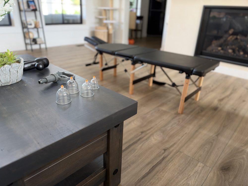 Suction cups, a hand pump and a massage gun on a coffee table, with the portable treatment table set up behind it