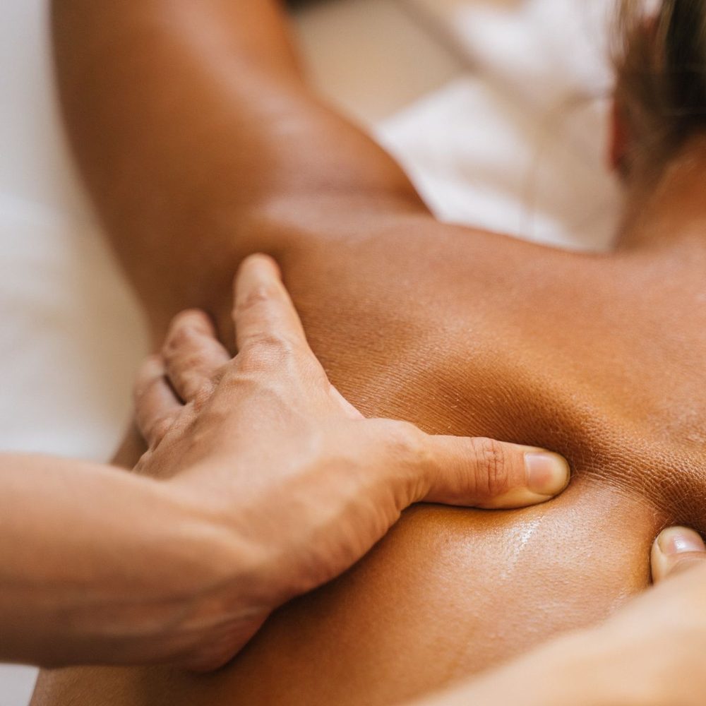 Hands working the muscle beside a patient's shoulder blade