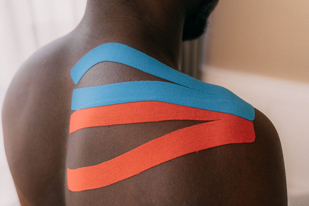 Blue and red kinesiology tape across a shoulder and upper back